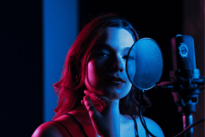 Una Mujer Frente al Microfono esperando usar La Plataforma Numero 1 de Distribucion con un fondo oscuro y Tonos neon Azul y Rosa